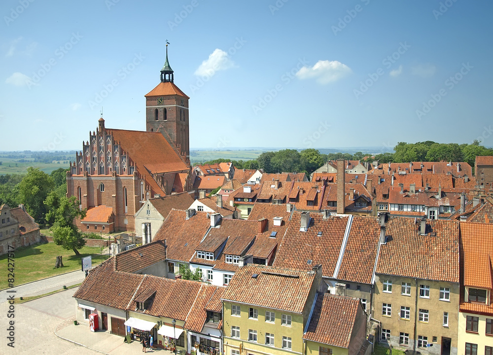 Fototapeta premium Old town and red brick medieval parish church of the St. Peter and Paul in Reszel, Poland. Wide sunny view with trees and blue sky. 