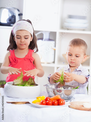 Two cute little children playing in the kitchen preparing salad