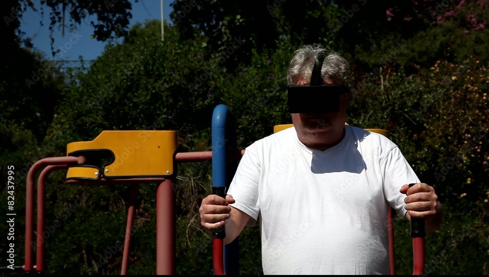 A big man with 3D VR head mounted display in outdoor gym, The athlete watches a movie while getting an exercise. A big man with 3D VR head mounted display in outdoor gym, The athlete watches a movie while getting an exercise.