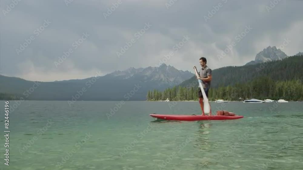 Wide shot of young man paddleboarding on lake / Redfish Lake, Idaho, United States Wide shot of young man paddleboarding on lake / Redfish Lake, Idaho, United States