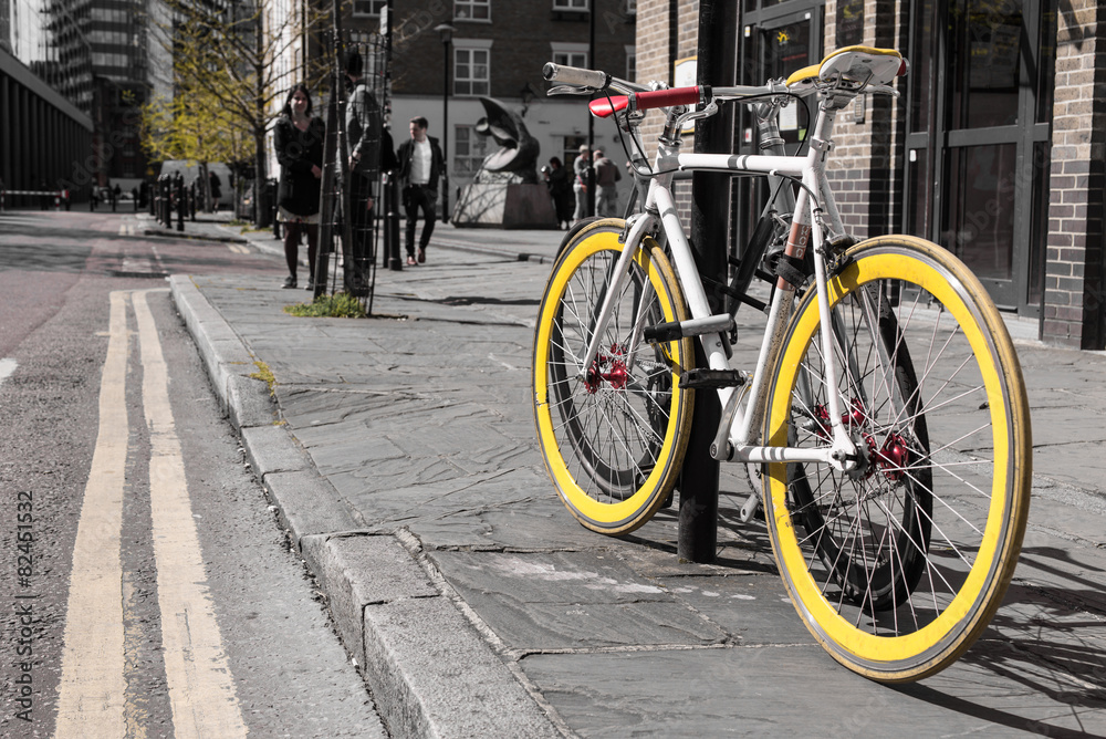 Modern single gear bycicle with yellow tyres locked to a lamp