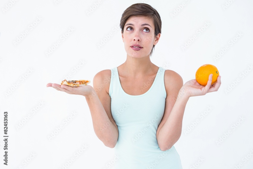 Woman choosing between pizza and an orange Woman choosing between pizza and an orange