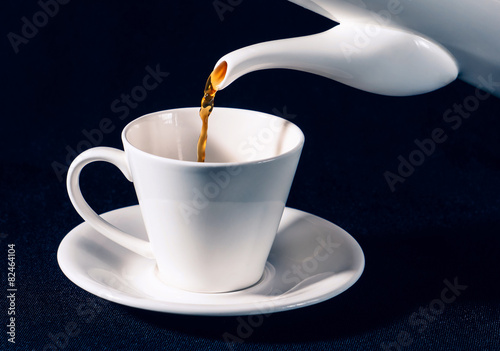 Pouring coffee from a pot into an empty white cup