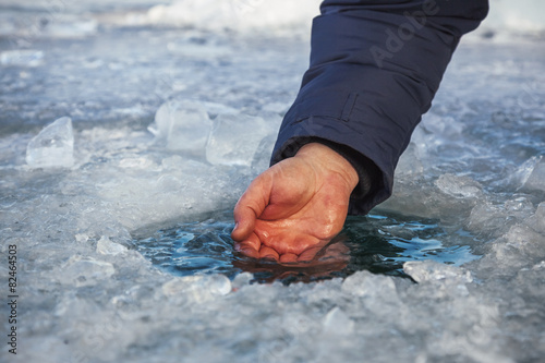 Male hand scoops water from the hole of the lake