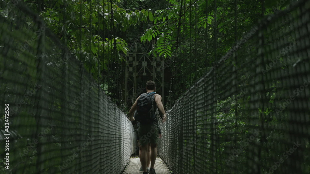 Wide shot of couple crossing hanging bridge in jungle / Arenal, Costa Rica