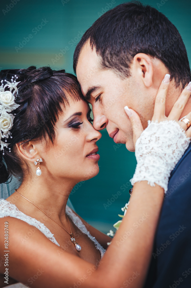 Young couple kissing in wedding gown. Bride holding bouquet of