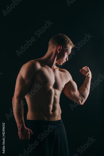 muscular young man showing his biceps isolated on black © satyrenko