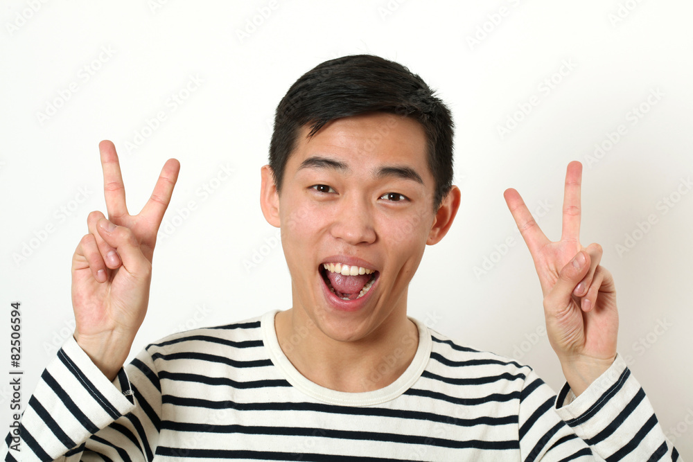 Laughing young Asian man giving two victory signs and looking at Laughing young Asian man giving two victory signs and looking at