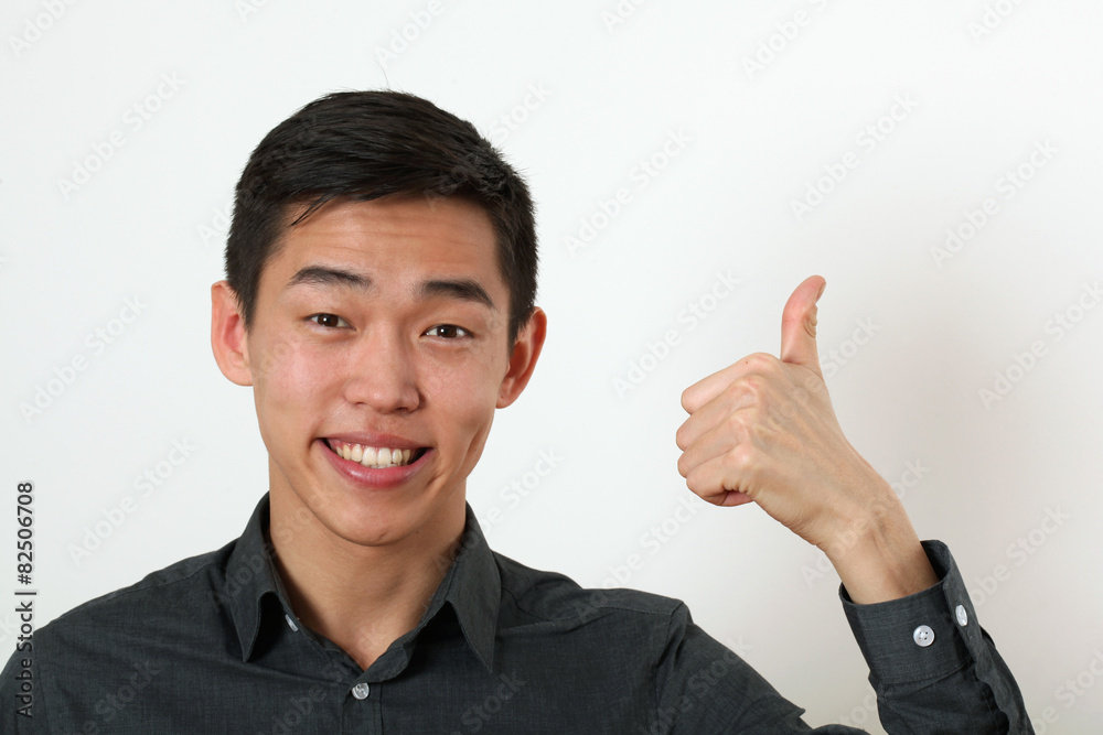 Smiling young Asian man giving the thumbs up signs and looking a Smiling young Asian man giving the thumbs up signs and looking a