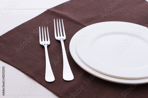 Empty plates  cutlery  tablecloth on white table for dinner.