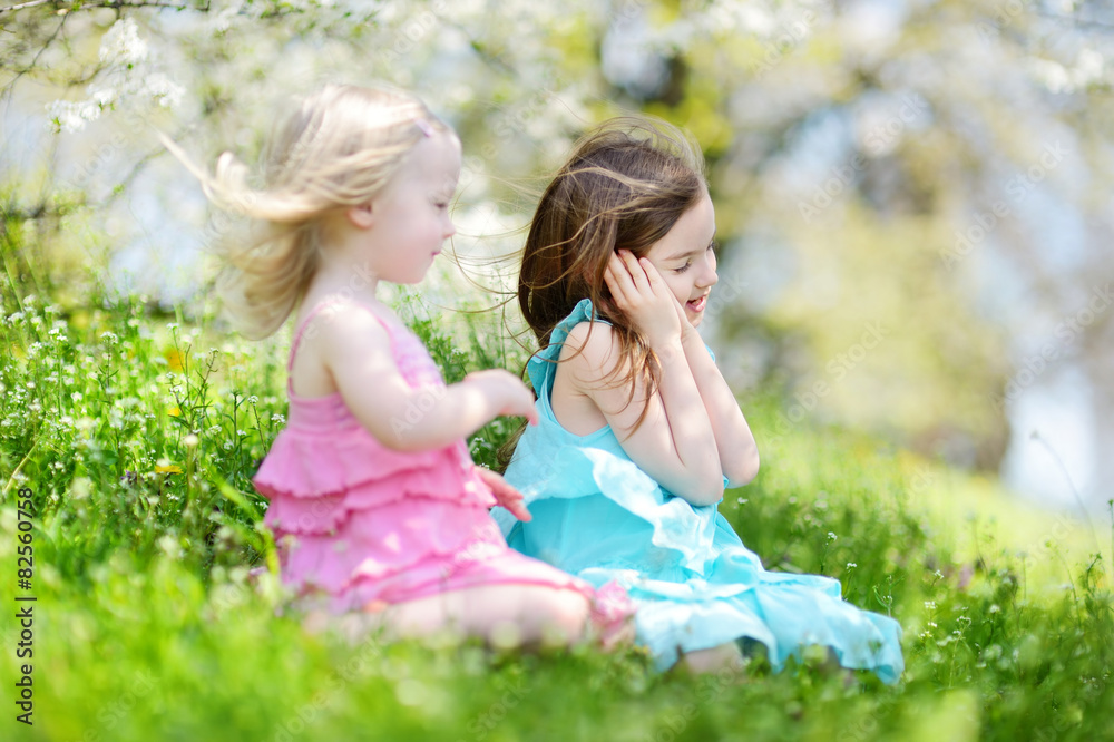 Two cute little sisters in blooming cherry garden Two cute little sisters in blooming cherry garden