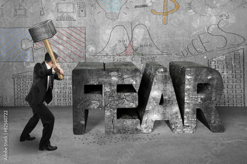 Businessman holding sledgehammer hitting fear concrete word with
