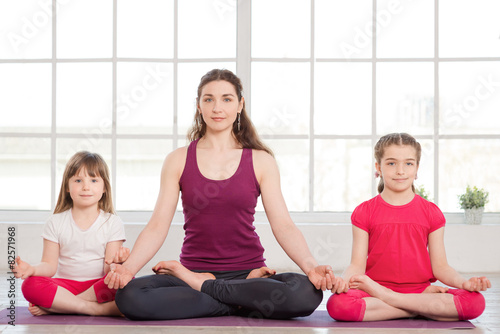Young mother and daughters doing yoga exercise