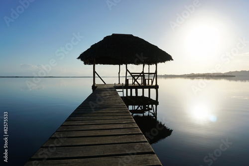 Dock with tropical hut over water on sunrise light