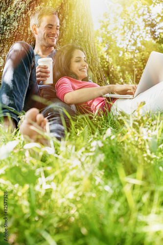 A nice couple sitting in the grass, using a laptop