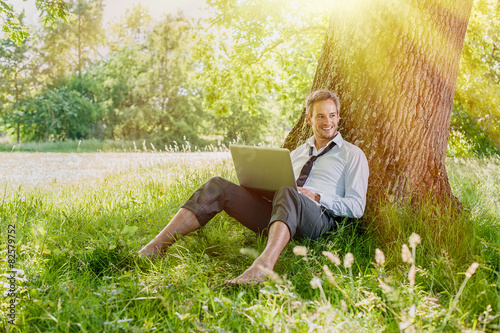 handsome grey hair man using a laptop, barefoot in the grass