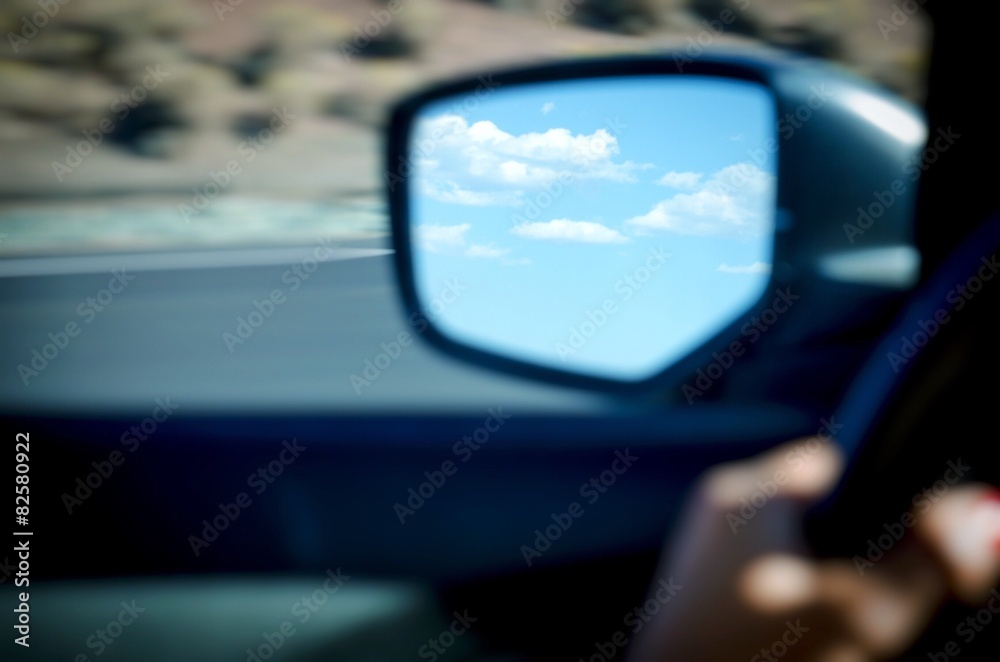 clouds in blue sky in rearview mirror of moving car