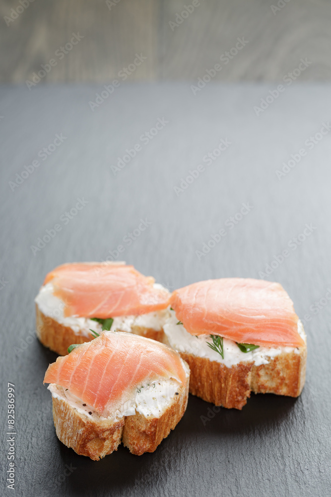 small sandwiches with soft cheese and salmon on slate background