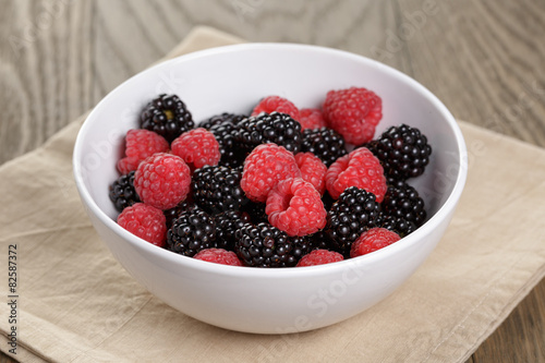 ripe blackberries and raspberries in white bowl on old oak table