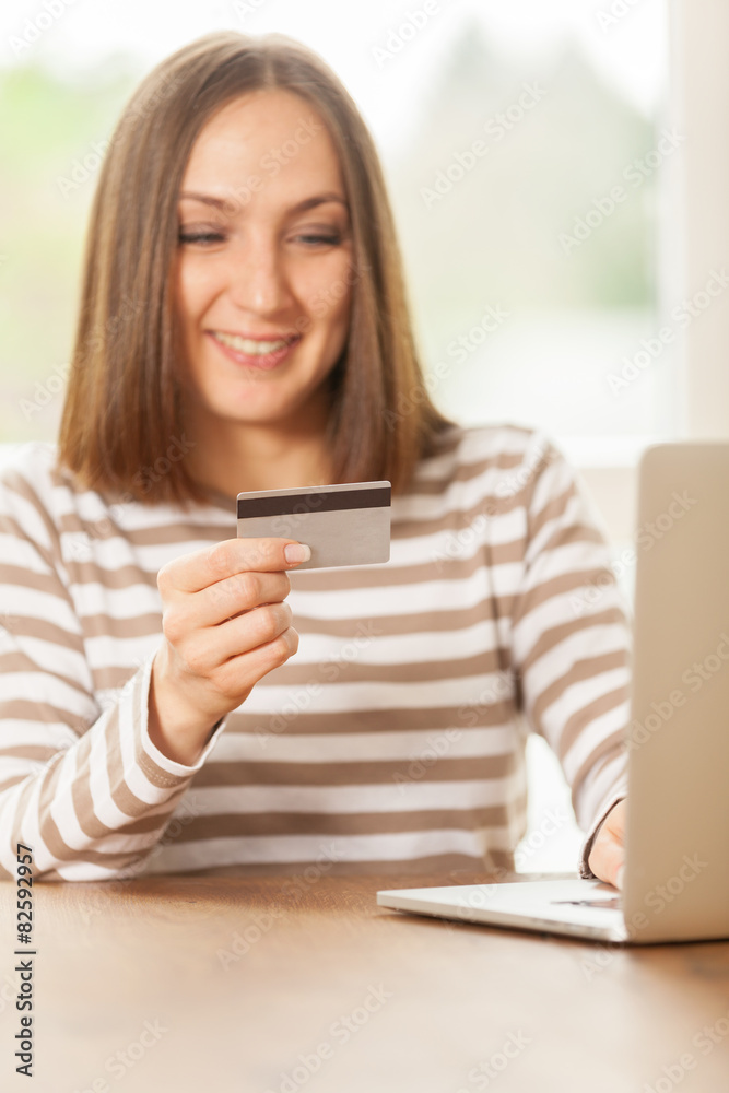 Young smiling woman holding a credit card in her hand while doin Young smiling woman holding a credit card in her hand while doin