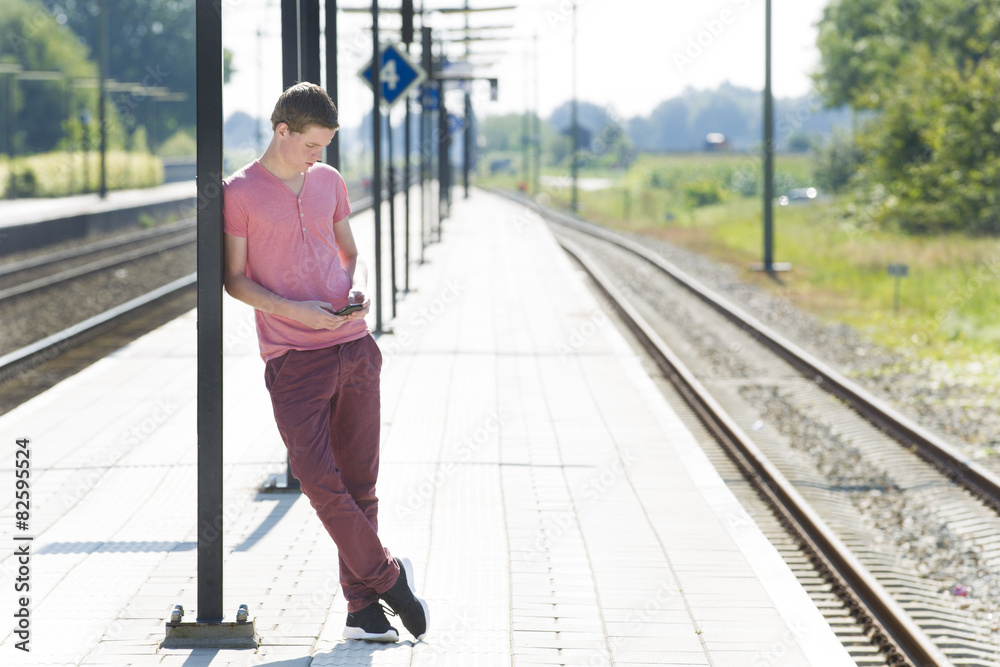 Man Using Mobile Phone While Waiting On Railway Platform Man Using Mobile Phone While Waiting On Railway Platform