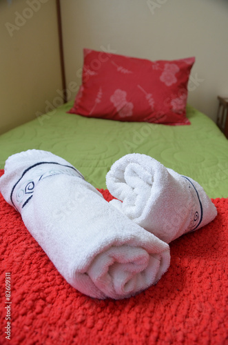 Rolled towels on hotel room bed with red cushion © lembrechtsjonas