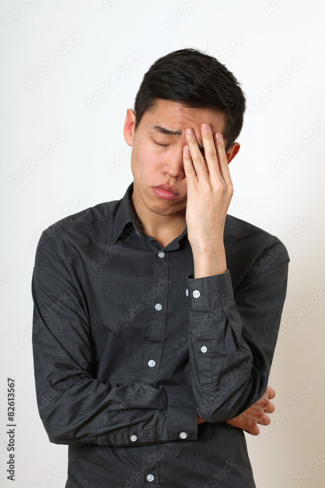Frustrated young Asian man covering his face with a palm Frustrated young Asian man covering his face with a palm