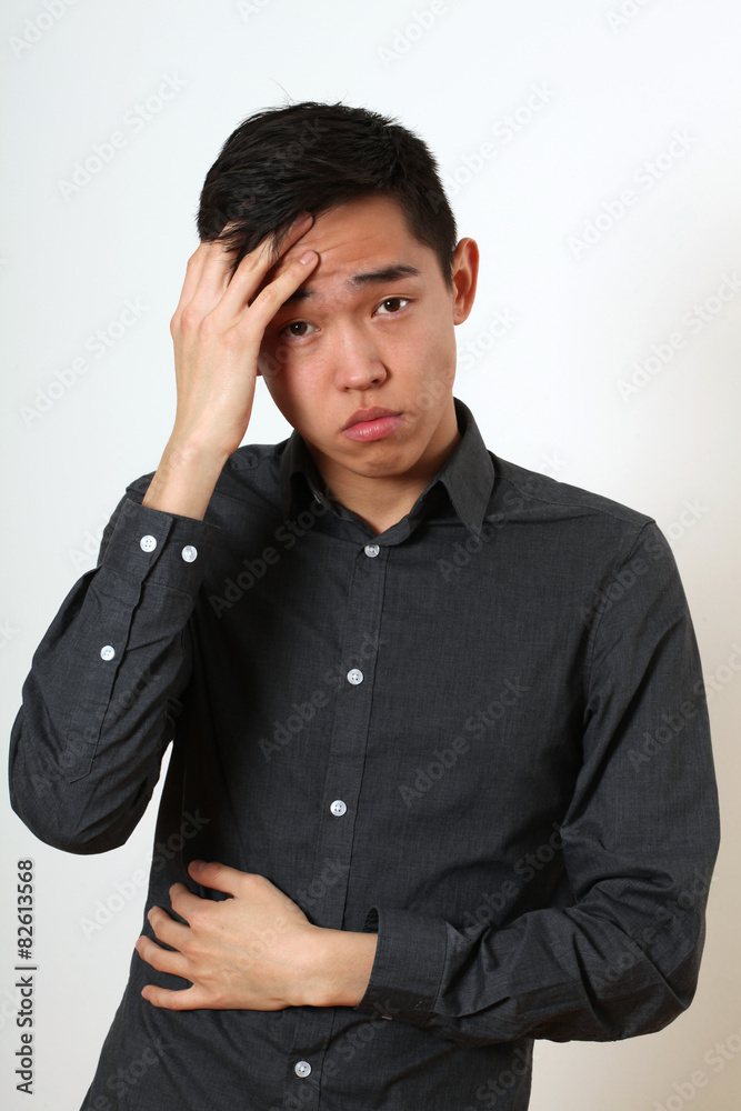 Frustrated young Asian man touching his forehead with his palm Frustrated young Asian man touching his forehead with his palm