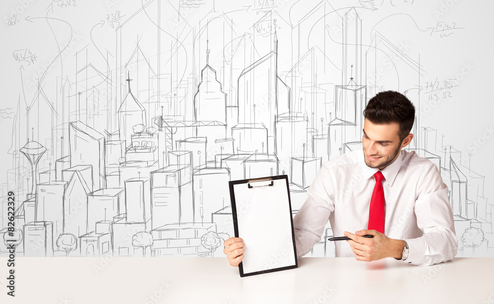 Businessman sitting at the white table with hand drawn buildings Businessman sitting at the white table with hand drawn buildings