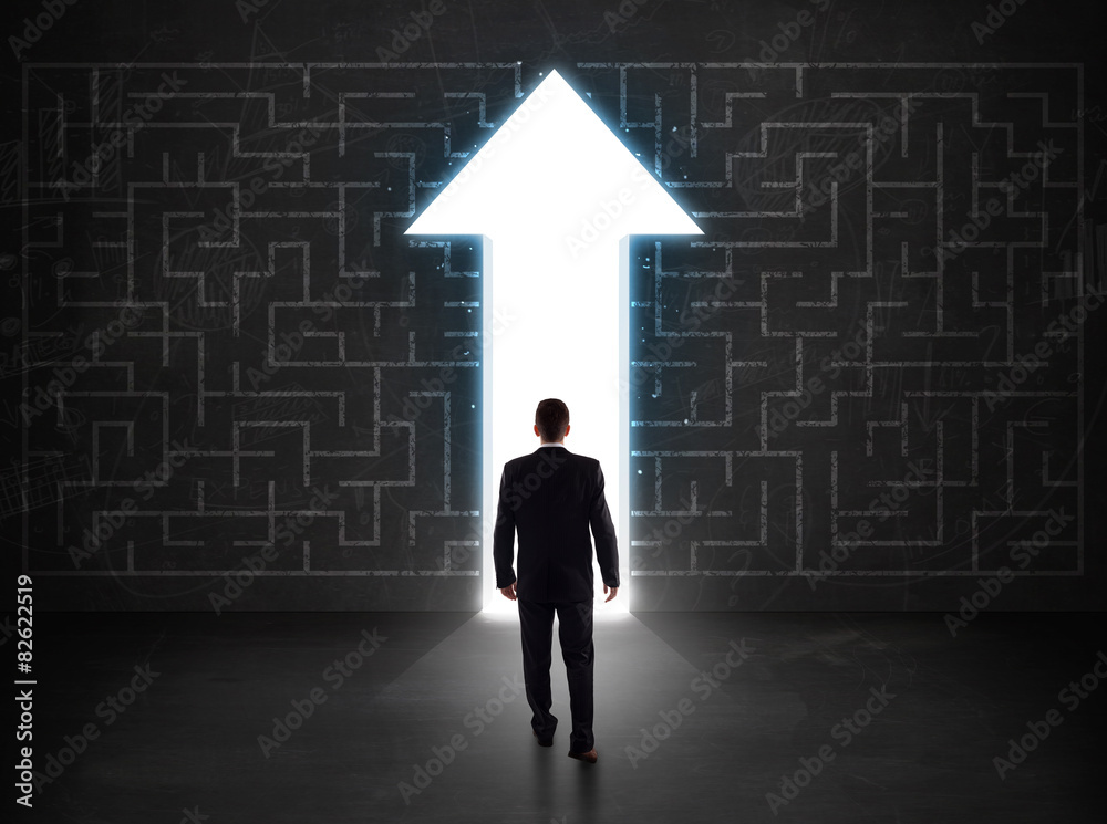 Business person looking at maze with solution arrow on the wall Business person looking at maze with solution arrow on the wall