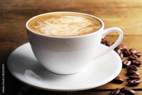 Cup of coffee latte art with grains on wooden table, closeup