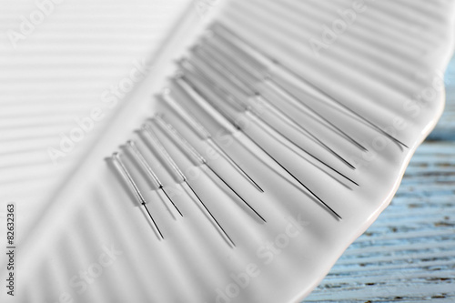 Acupuncture needles on plate on wooden table, closeup