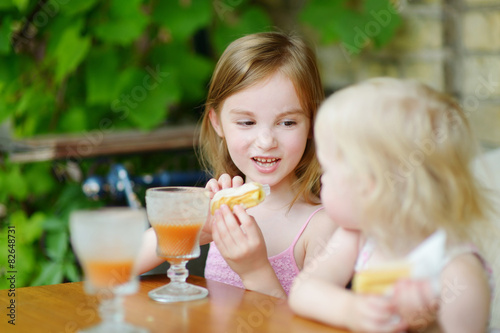 Two sisters drinking juice and eating pastries