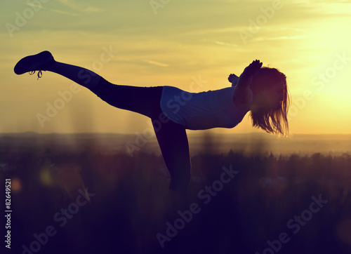 Fototapeta Naklejka Na Ścianę i Meble -  Silhouette of young woman stretching on a meadow at sunset