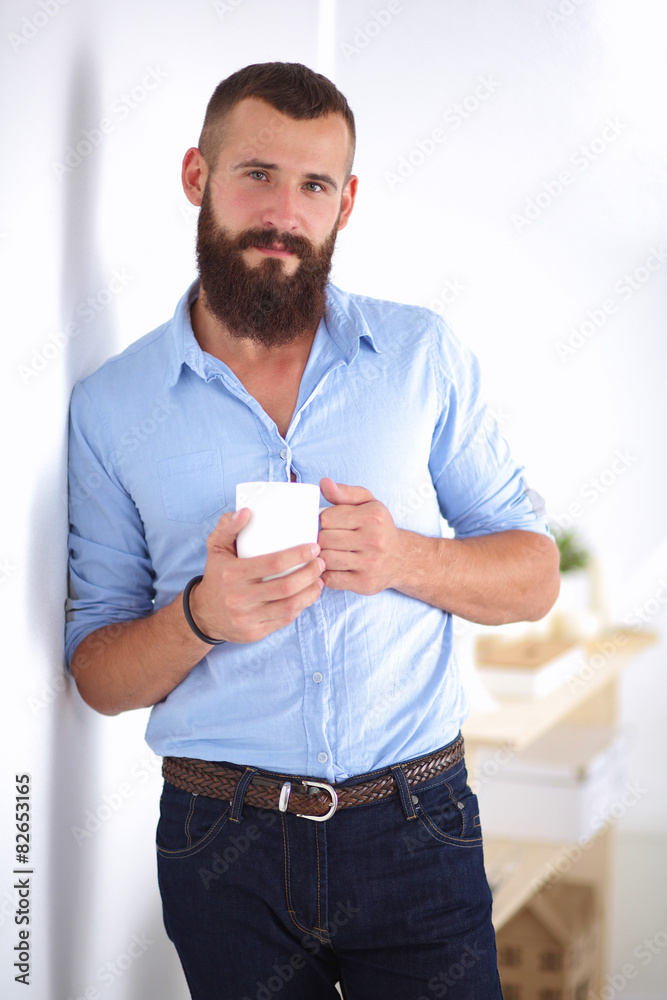 Young man standing near wall and holding cup of coffee in Young man standing near wall and holding cup of coffee in