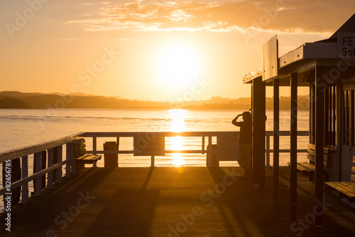 A woman standing at a pier and looking into the distance at suns