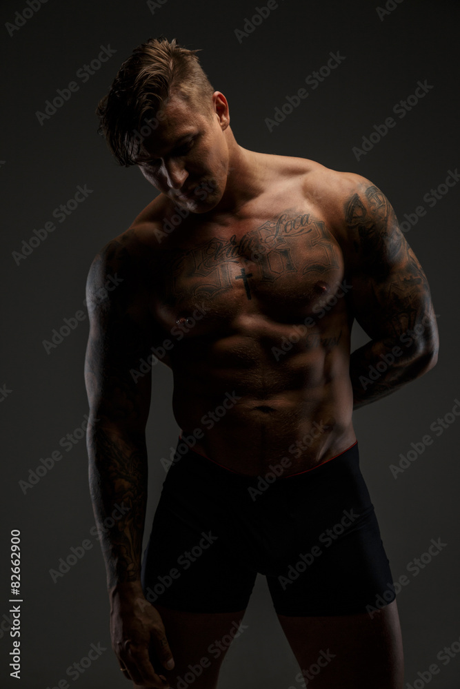 Fototapeta premium Muscular man with tattooes in deep shadows