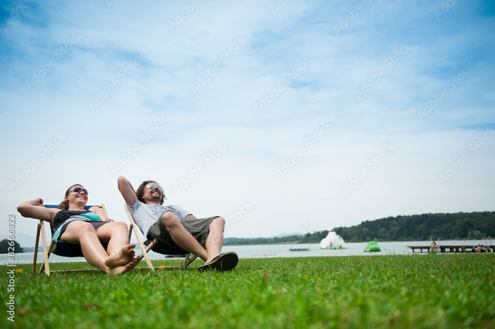 Junges Paar entspannt in der Sonne im Liegestuhl am See