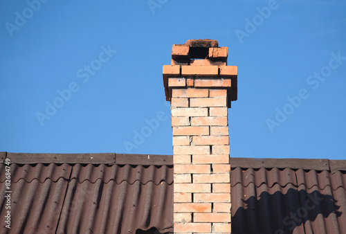 Roof of rural house with smoke pipe from bricks over blue sky