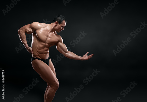 Slika na platnu Handsome muscular bodybuilder posing over black background.