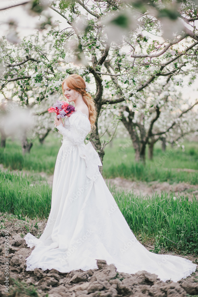 Young woman in vintage wedding dress posing in blooming garden