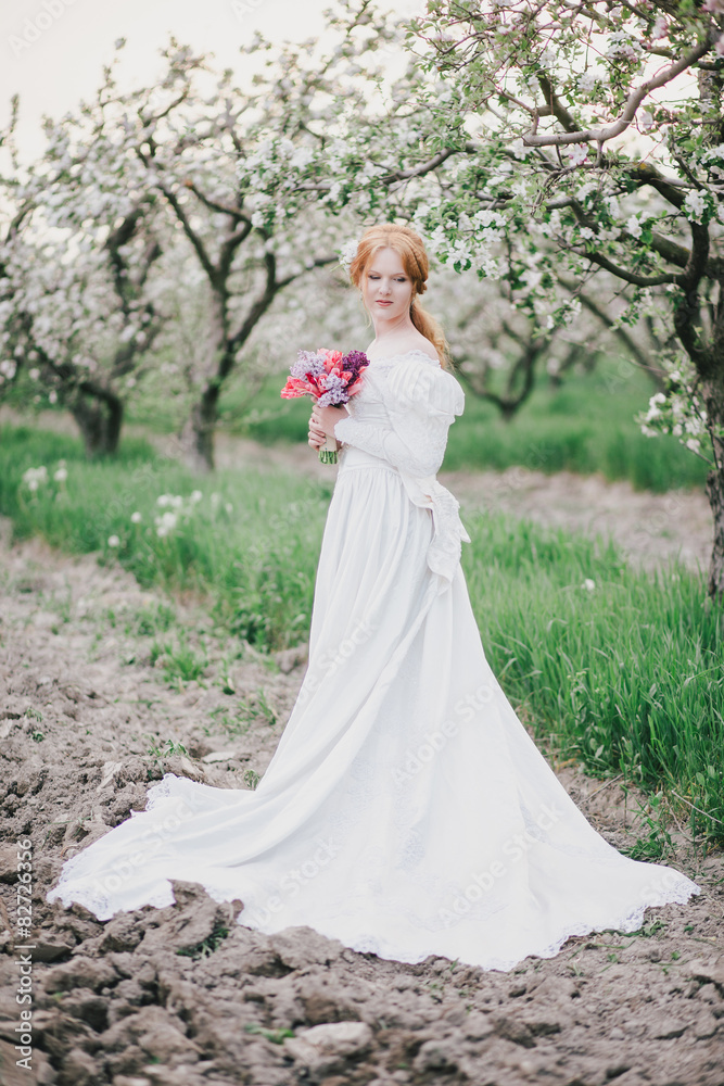 Young woman in vintage wedding dress posing in blooming garden