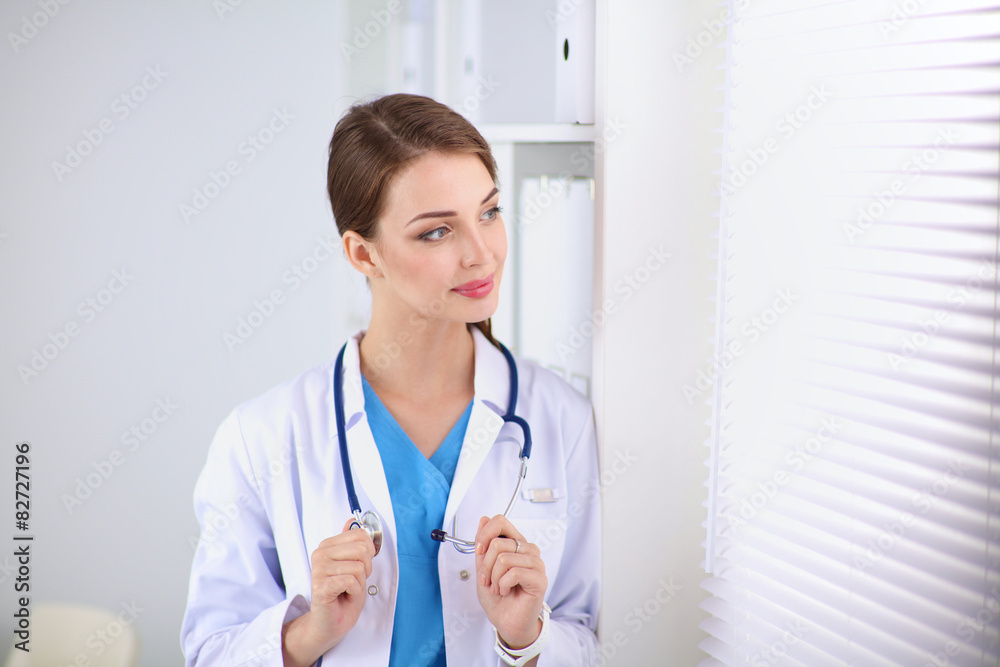 Woman doctor is standing near window with crossed arms,isolated Woman doctor is standing near window with crossed arms,isolated