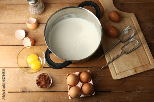 Preparation cream with eggs in pan on wooden background