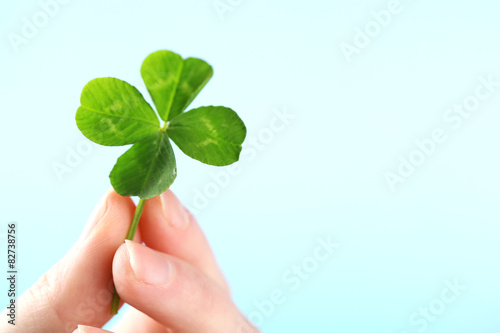 Female hand holding green clover leaf on sky background