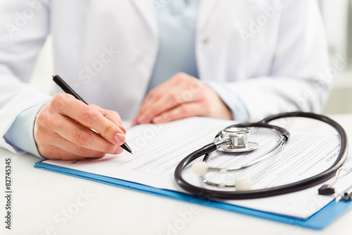 Young woman physician with stethoscope prescribing treatment 
