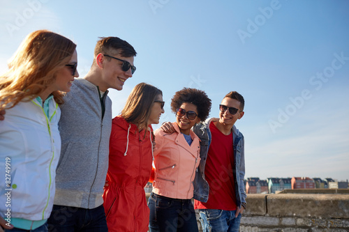 happy teenage friends walking along city street