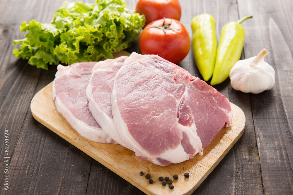 Raw pork on cutting board and vegetables on wooden background Raw pork on cutting board and vegetables on wooden background