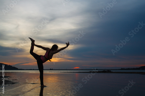 Silhouette of young woman practicing yoga on the lake at sunset