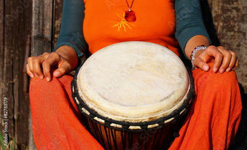 Young lady drummer with her djembe drum on rustic wooden door 